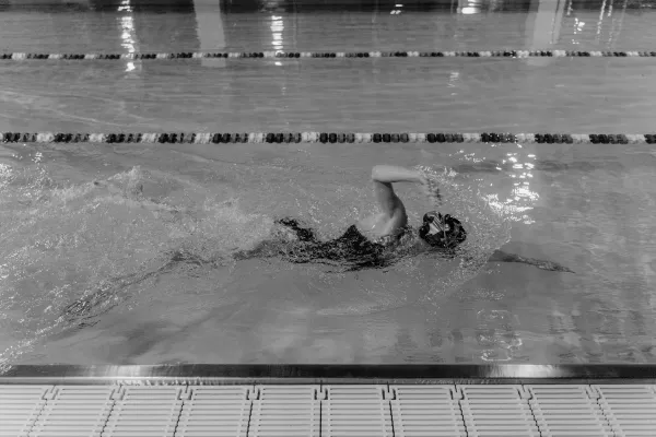 Nageur en crawl dans une piscine intérieure, photographié en noir et blanc.