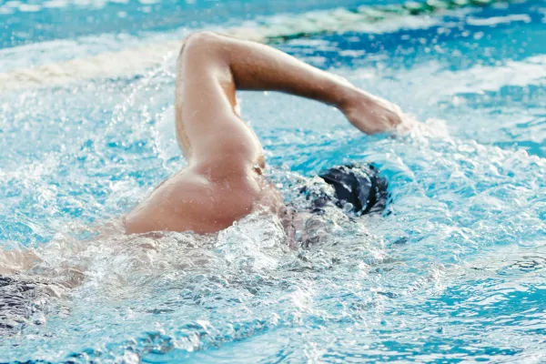 Nageur en crawl régulier dans une piscine extérieure.