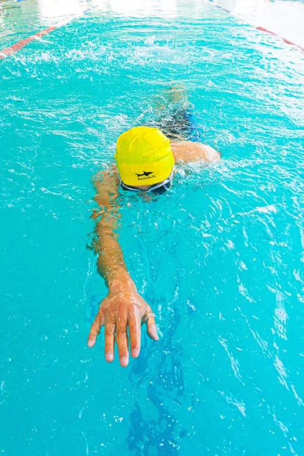 Nageur en bonnet jaune travaillant son crawl dans une piscine intérieure.