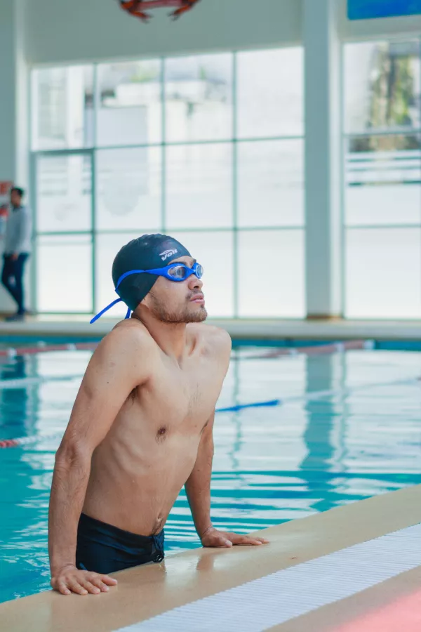 Nageur faisant une pause au bord d’une piscine intérieure, bonnet et lunettes en place.