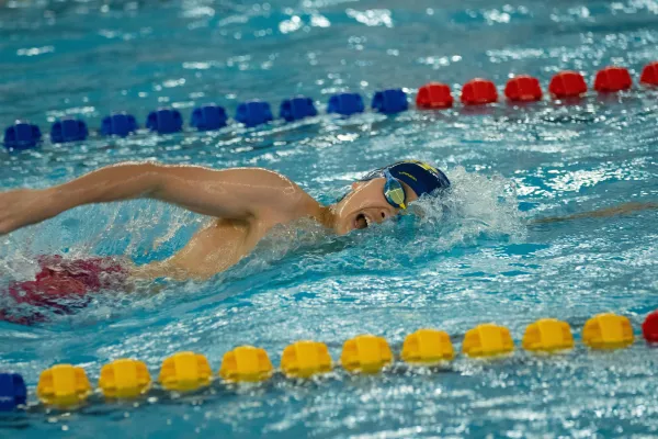 Nageur en crawl rapide dans un couloir de piscine intérieure.