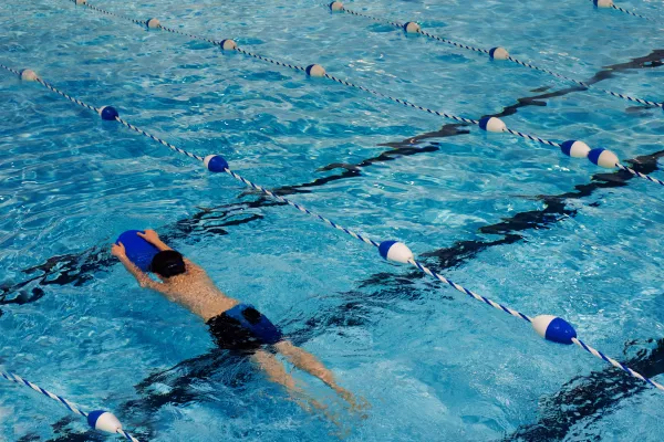 Jeune nageur travaillant les battements avec une planche dans un couloir de piscine.