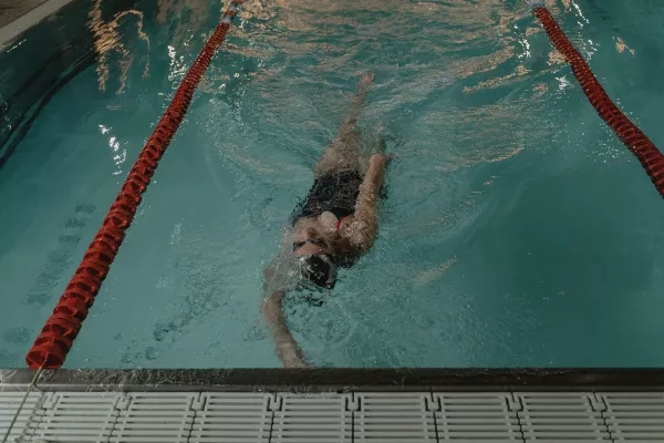 Nageuse effectuant le dos dans un couloir de piscine intérieure.