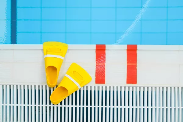 Paire de palmes jaunes posée au bord d’une piscine.