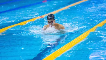 Nageur effectuant la brasse dans un couloir de piscine intérieure.