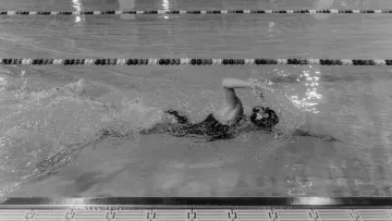 Nageur en crawl dans une piscine intérieure, photographié en noir et blanc.