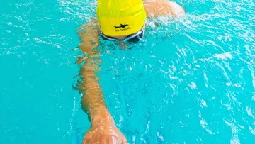 Nageur en bonnet jaune travaillant son crawl dans une piscine intérieure.