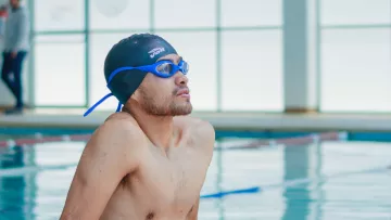 Nageur faisant une pause au bord d’une piscine intérieure, bonnet et lunettes en place.