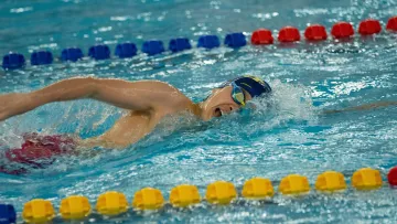 Nageur en crawl rapide dans un couloir de piscine intérieure.