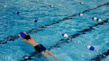 Jeune nageur travaillant les battements avec une planche dans un couloir de piscine.
