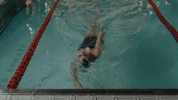 Nageuse effectuant le dos dans un couloir de piscine intérieure.