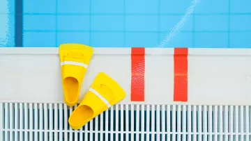 Paire de palmes jaunes posée au bord d’une piscine.